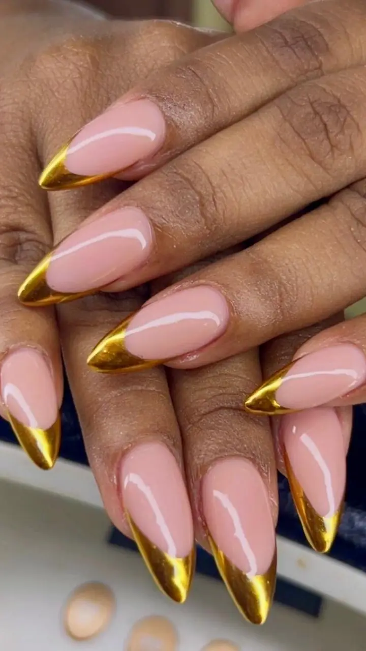 A finished set of almond extensions with gold chrome tips, photographed at the nail desk.