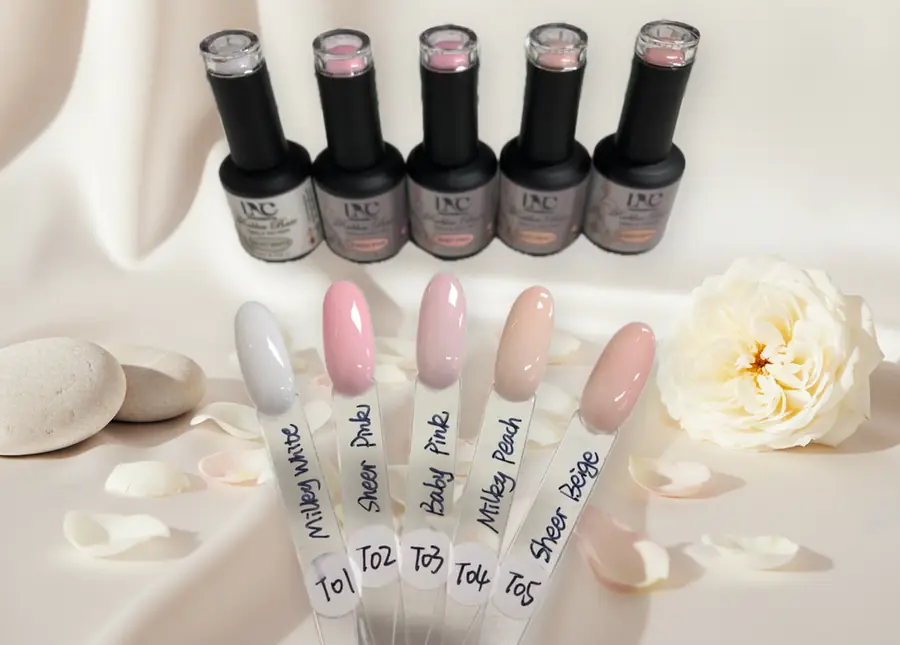 Five LNC Professional Rubber Base bottles beside hand-labelled swatch sticks showing the sheer and milky shades.