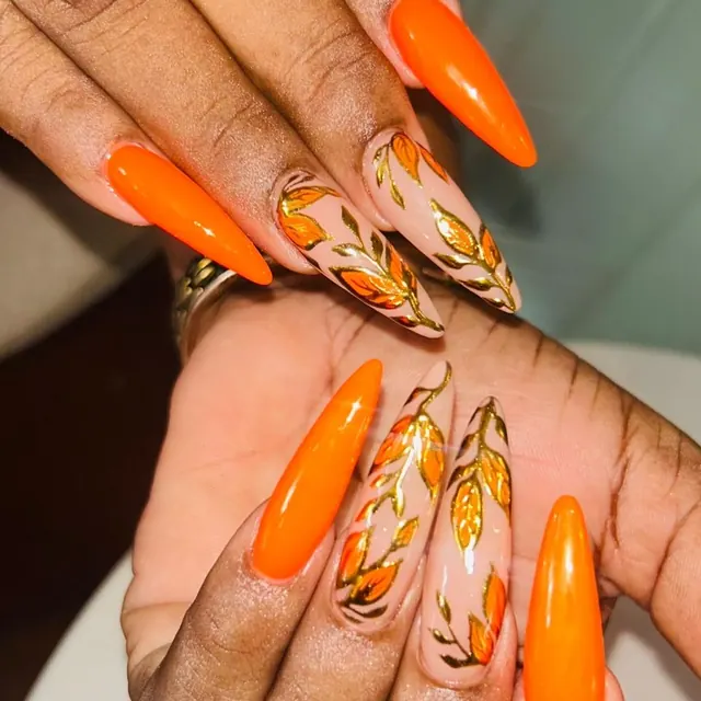 Long stiletto extensions in bright orange with hand-painted detail.